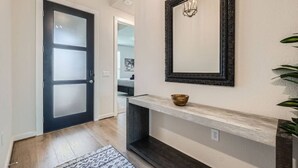A hallway with a dark door, a light wall, a mirror, and a small shelf with a bowl.
