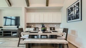 A dining area with a large table, benches, and a kitchen in the background.