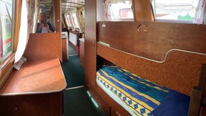 A train compartment with wooden bunk beds, a small table, and a window with curtains. - Stone - Self-drive Boat - Sleeps 8 - Pet Friendly (Stone)