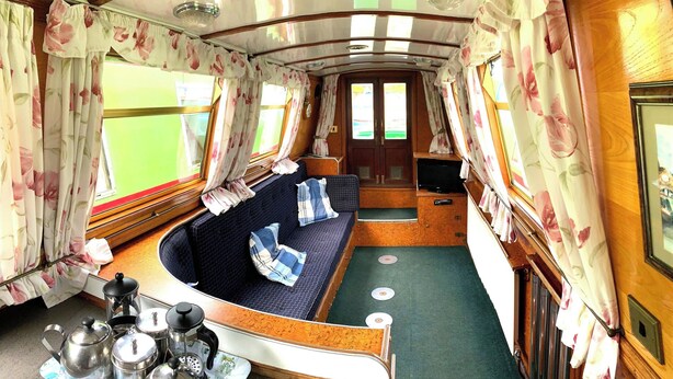 A cozy interior with a sofa, a small table with kitchen items, and floral curtains. - Stone - Self-drive Boat - Sleeps 8 - Pet Friendly (Stone)