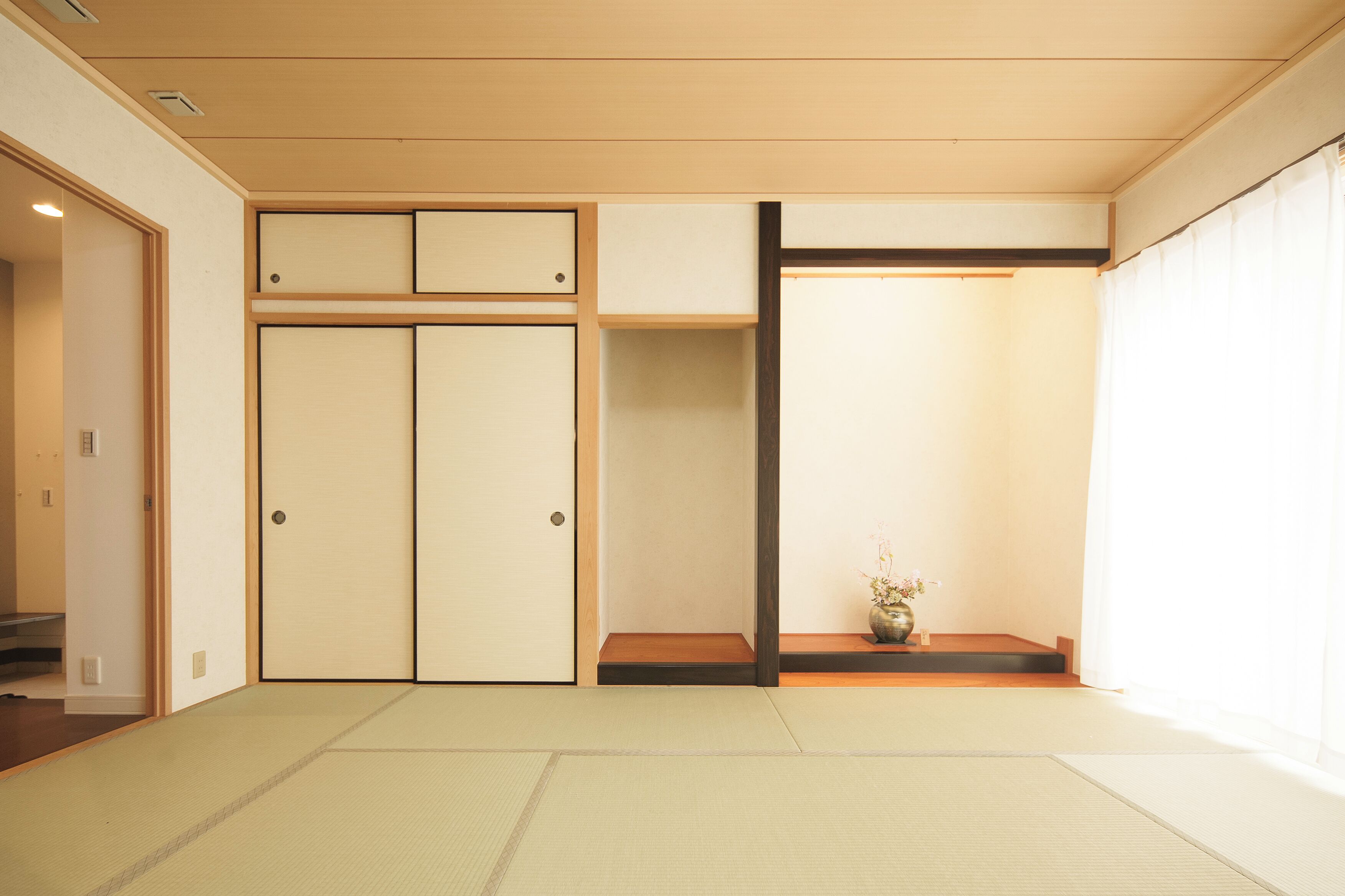 Une pièce de style japonais traditionnel, avec un sol recouvert de tatamis, des portes coulissantes et une petite table sur laquelle est posé un vase.