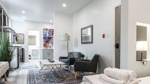 A modern living room with a sofa, a coffee table, and a rug. There is a painting on the wall and a lamp on the side table. - The Hawthorne Apartment (Stratford)
