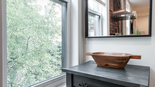 A kitchen with a large window, a wooden bowl on a dark countertop, and a modern stove. - The Hawthorne Apartment (Stratford)