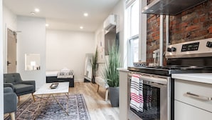 A modern kitchen with a brick wall, a large stove, and a dining area with a sofa and coffee table. - The Hawthorne Apartment (Stratford)