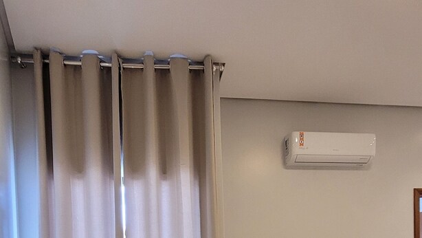 A bedroom with a bed, curtains, an air conditioner, and a small table.