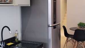 A modern kitchen with a stainless steel refrigerator, a built-in microwave, and a sink with a faucet. There is a dining area with a table and chairs in the background.