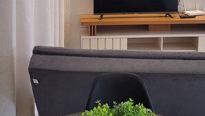 A modern living room with a flat-screen TV on a wooden stand, a grey sofa, and a table with a crocheted plant centerpiece.