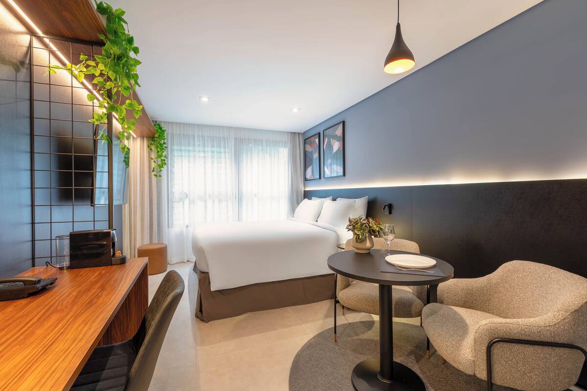 Una habitación de hotel moderna con una cama grande, un escritorio de madera, una mesa redonda y un sofá.