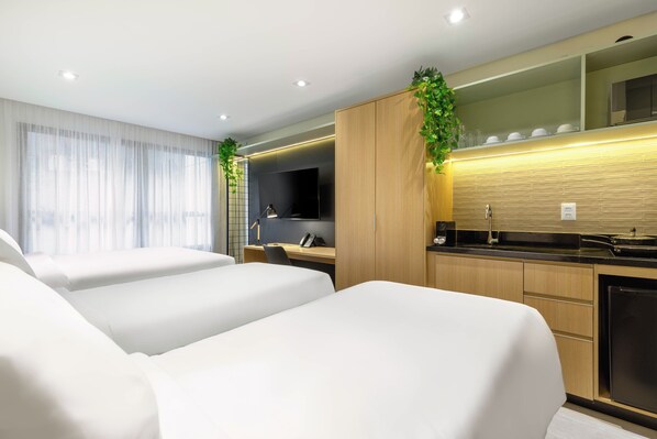 Una habitación de hotel moderna con dos camas, un escritorio, un televisor y una zona de cocina.