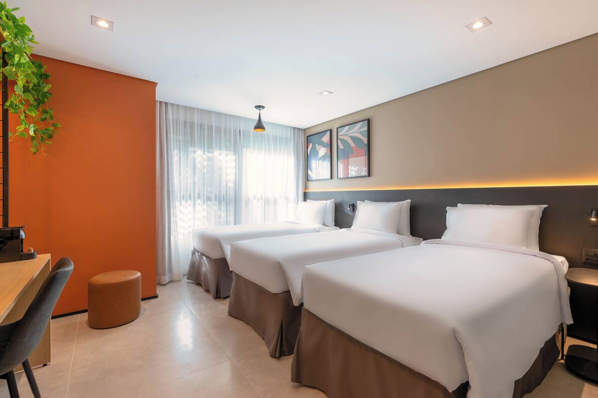 Habitación de hotel con tres camas, un escritorio, una silla y un pequeño taburete redondo.