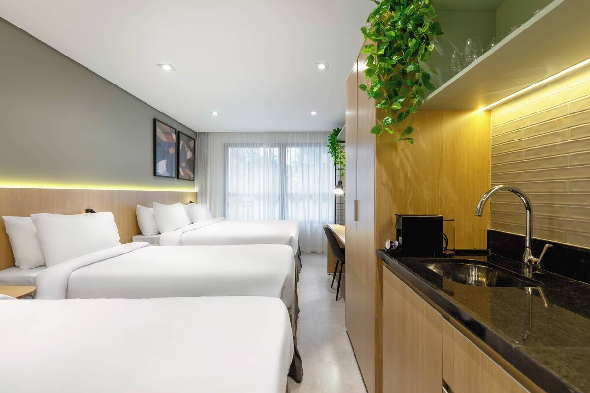 Habitación de hotel con tres camas, kitchenette y vista a la ciudad.