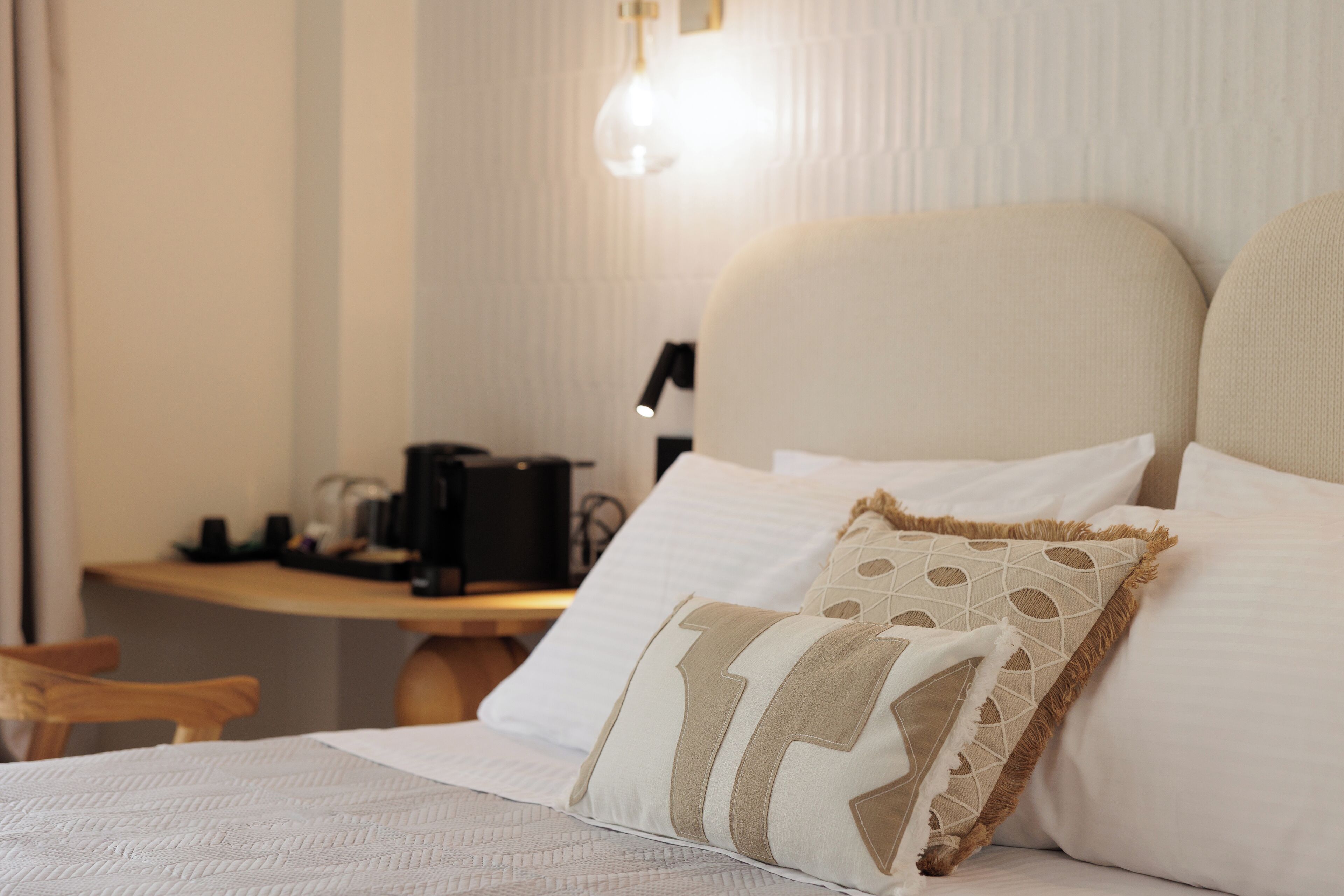 A neatly made bed with a patterned pillow, a bedside table with a lamp, and a wall-mounted light fixture.