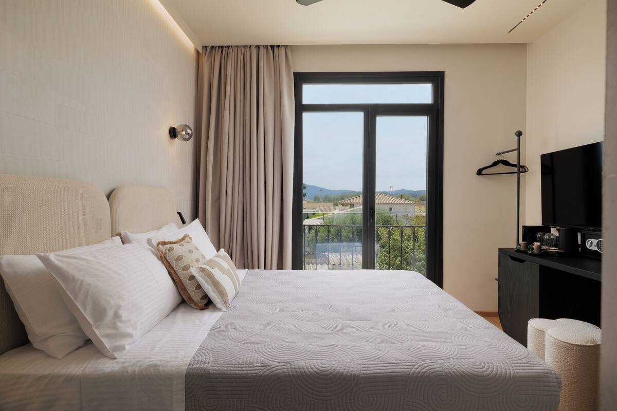 A bedroom with a large bed, a TV, a wardrobe, and a balcony with a view.