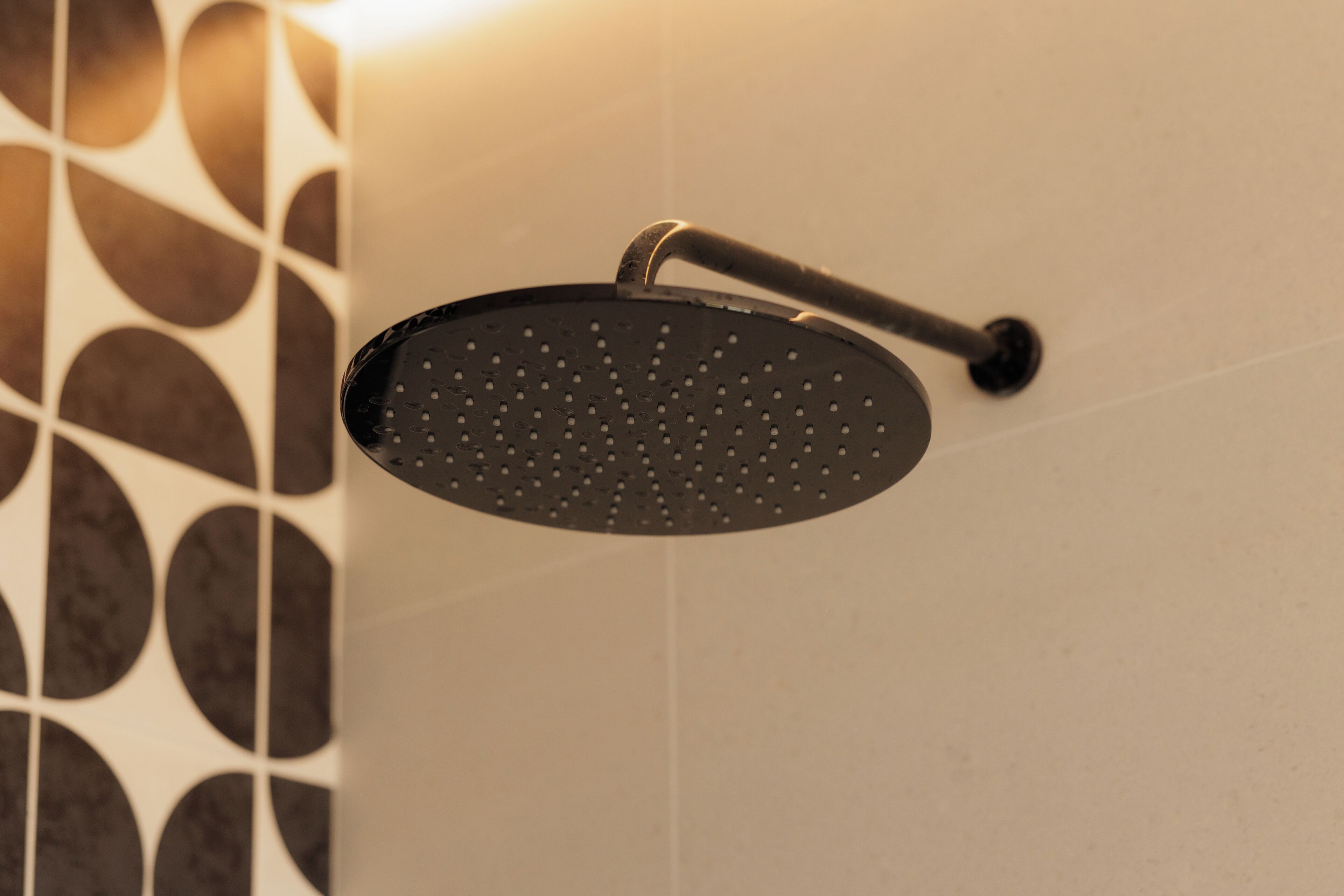 A showerhead with a curved design, mounted on a wall with a geometric tile pattern.
