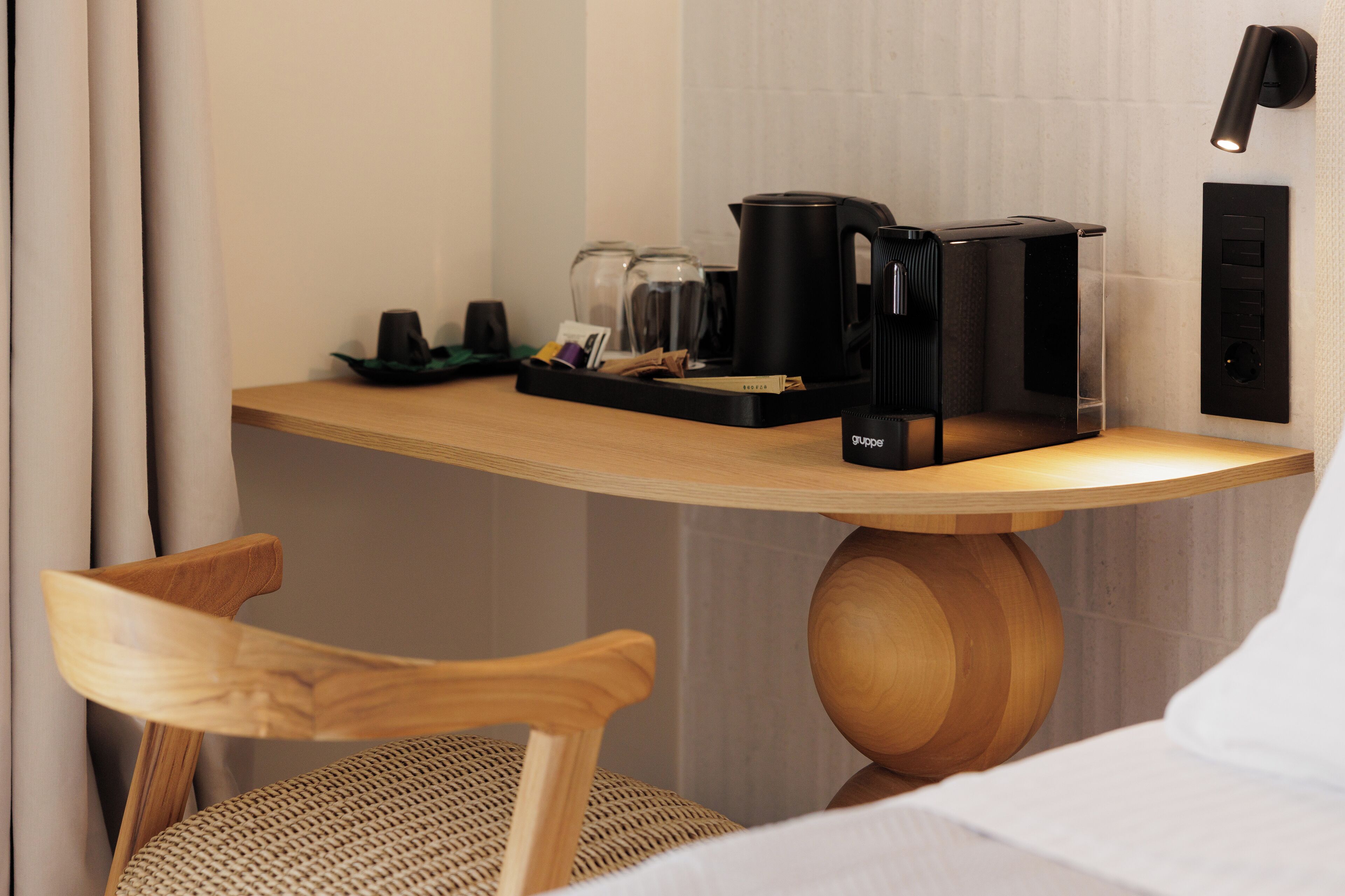 Habitación de hotel con escritorio de madera, cafetera negra, hervidor y bandeja con objetos.