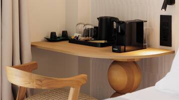Habitación de hotel con escritorio de madera, cafetera negra, hervidor y bandeja con objetos.