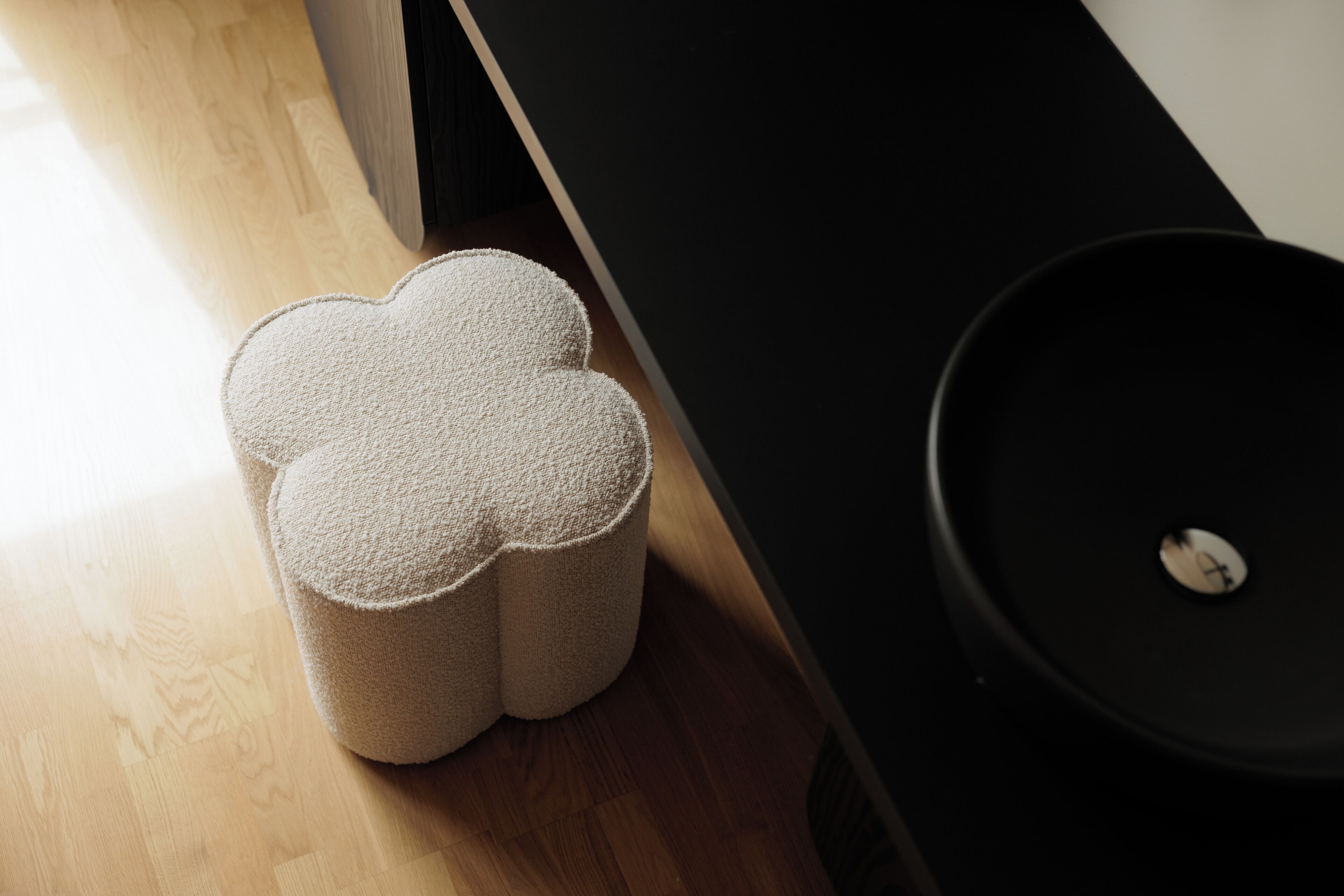 A room with a wooden floor, a black cabinet, and a beige, textured ottoman with a unique shape.