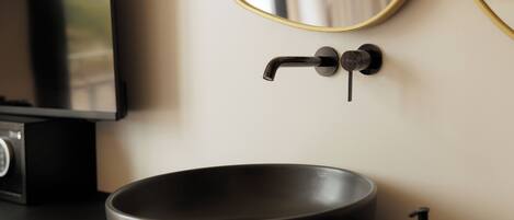 A modern bathroom with a black sink, a faucet, a mirror, and a soap dispenser.