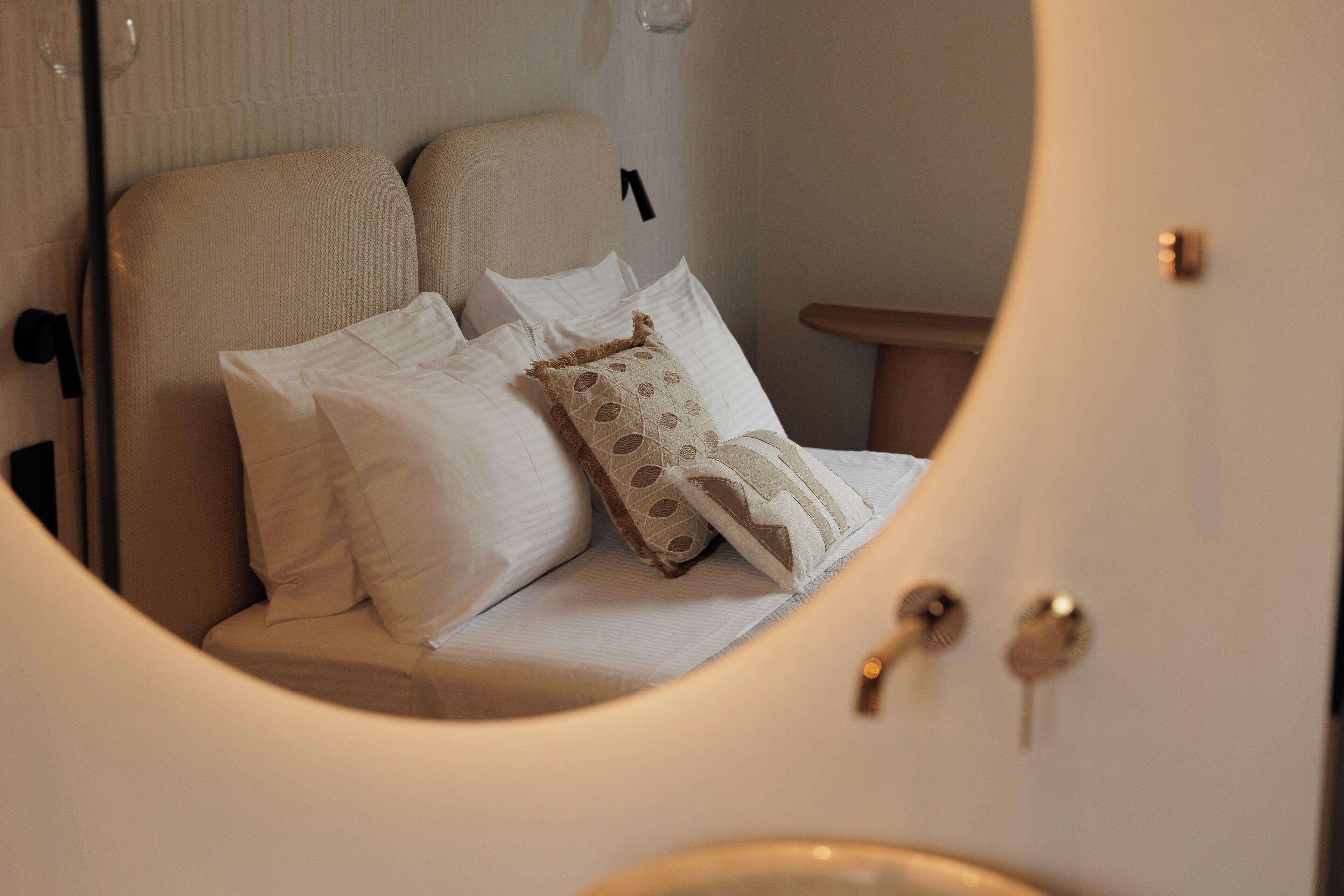 Una cama con ropa de cama blanca y almohadas estampadas, una mesita de noche y una lámpara de pared.