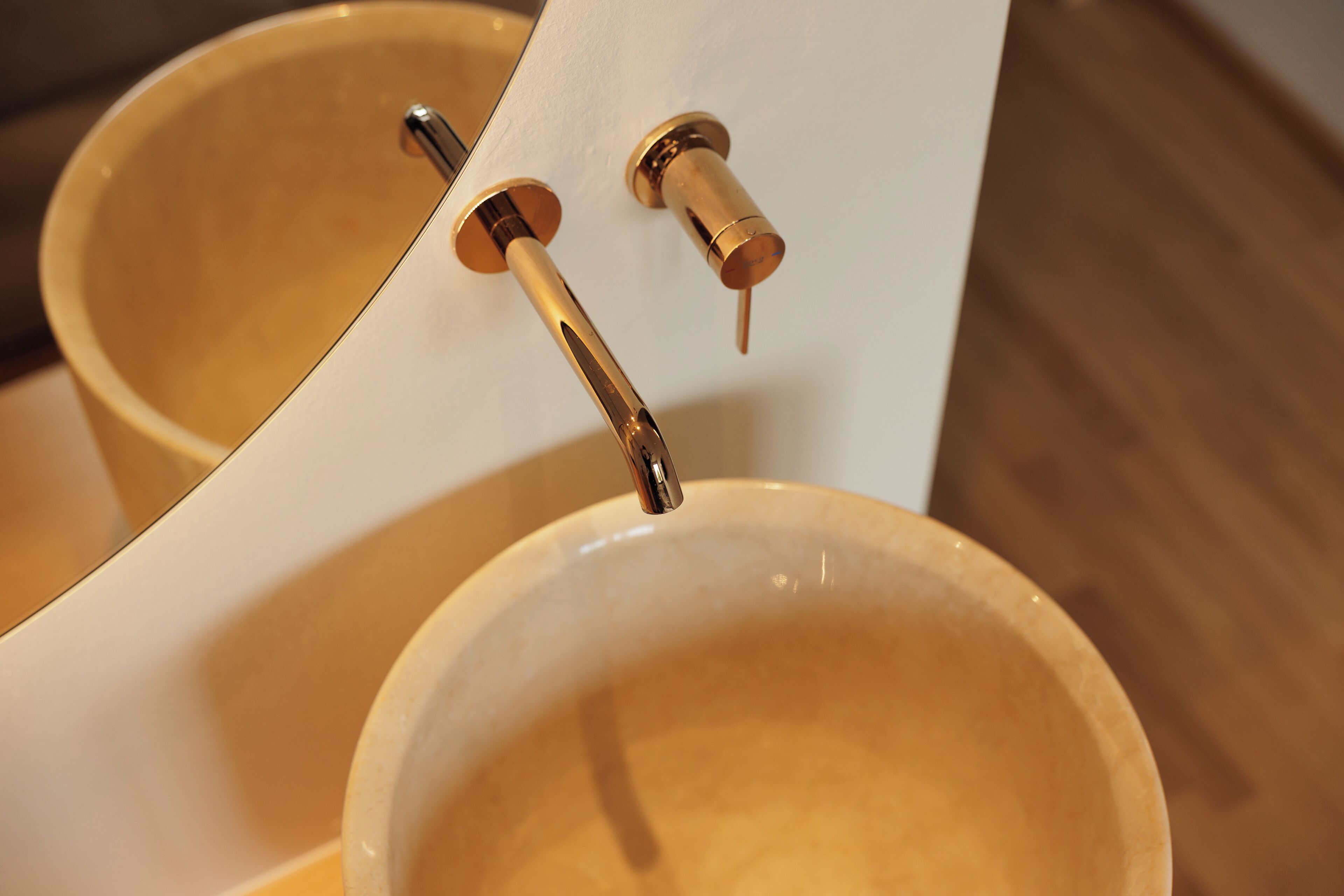 Ein Detailaufnahme von einem Badezimmerwaschbecken mit einem goldenen Wasserhahn und einem Spiegel darüber.