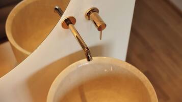 Ein Detailaufnahme von einem Badezimmerwaschbecken mit einem goldenen Wasserhahn und einem Spiegel darüber.