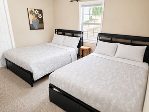 Two twin beds with matching headboards and footboards, a small wooden stool, a window with a view of greenery, and a painting on the wall. - Slice of Paradise- Ramp nearby/Secured boat/trailer parking for $15 (Gravois Mills)