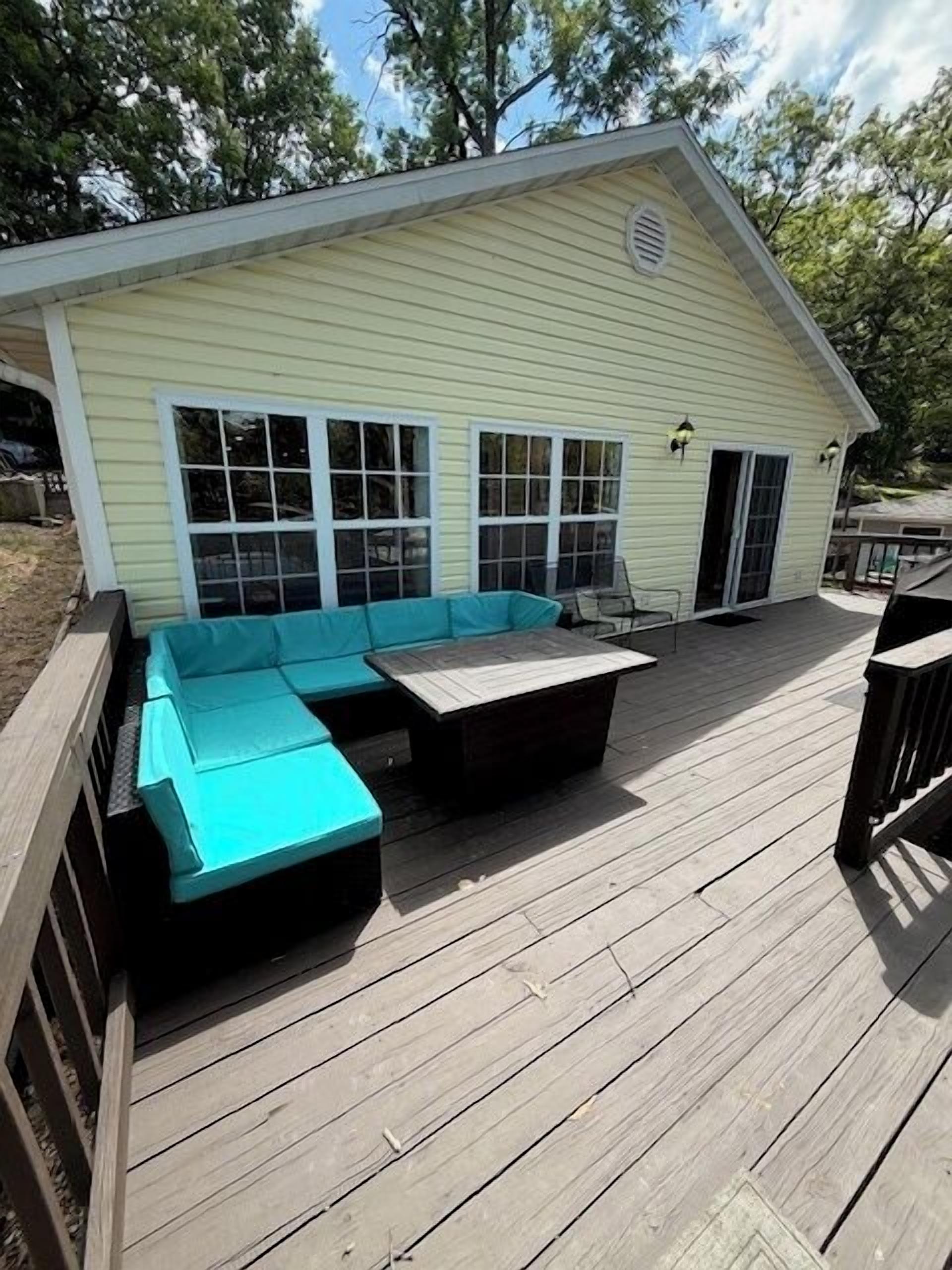 A covered deck with a turquoise sofa and a wooden table.
