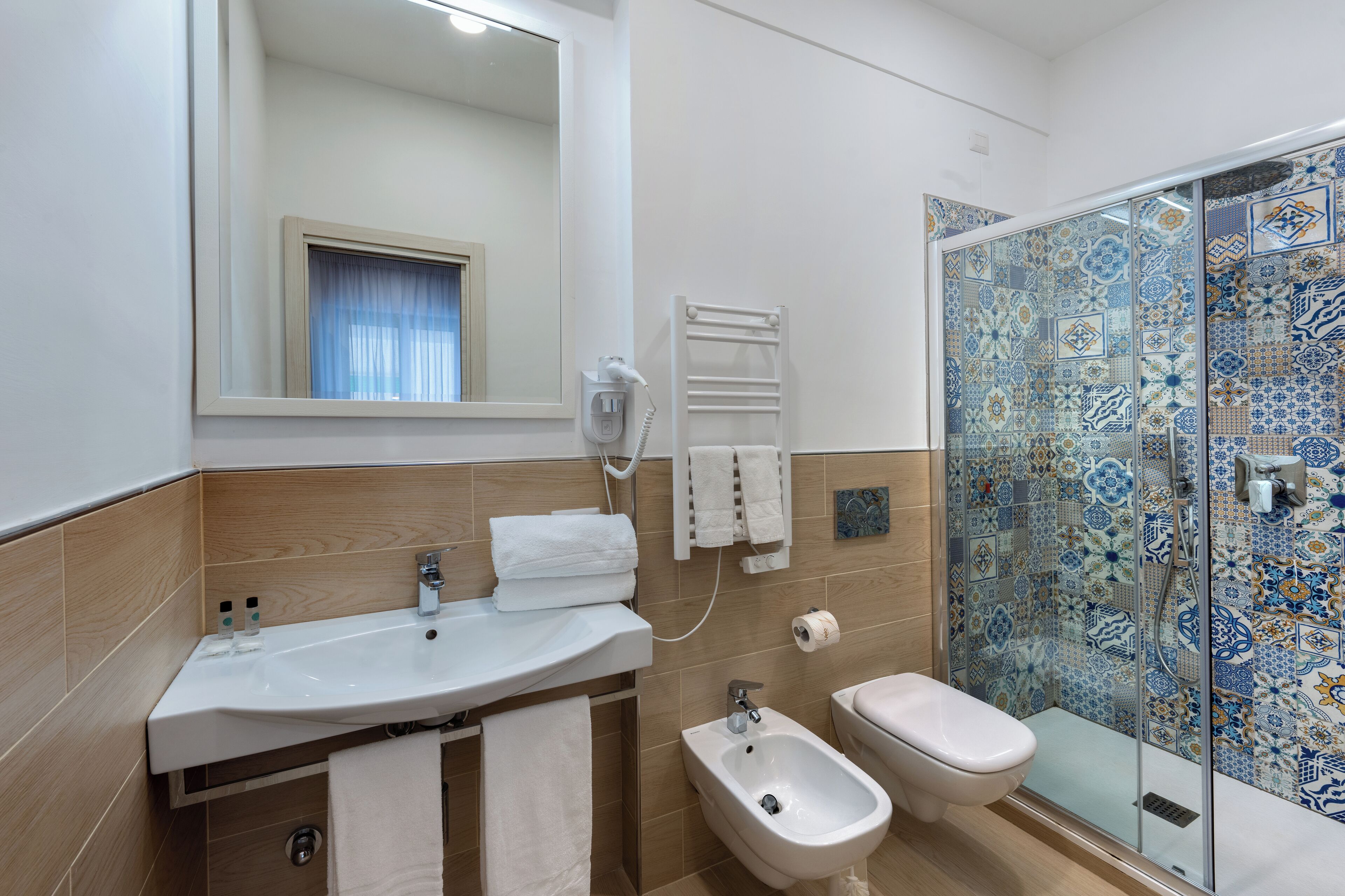 Un baño moderno con lavamanos, bidé, inodoro y ducha con azulejos estampados.