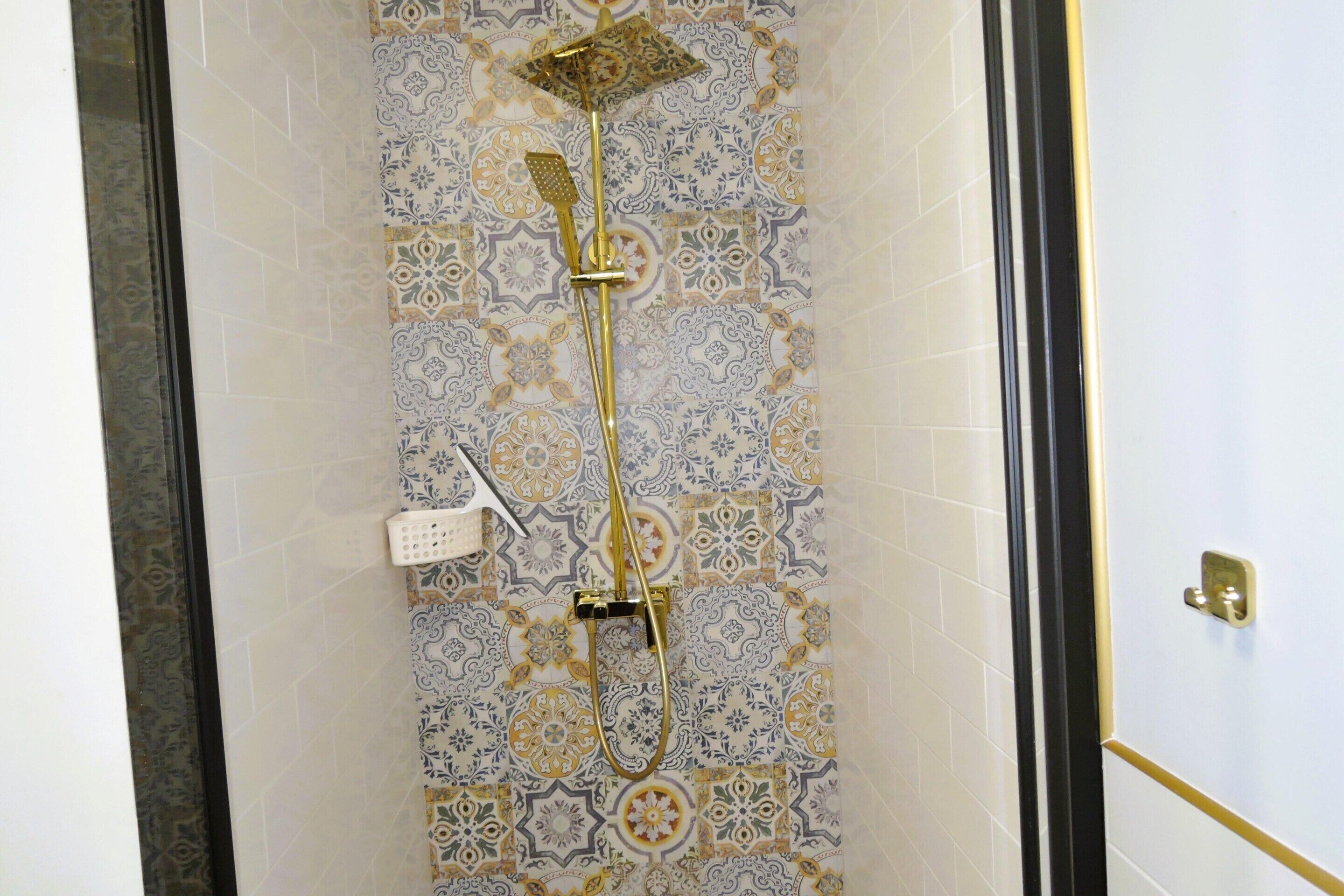 A shower with a gold showerhead and control panel, set against a patterned tile wall.