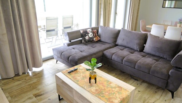 A modern living room with a sectional sofa, a wooden coffee table with a floral runner, and a dining area in the background. - Luxury Holiday Home for 20 People (gmina Wolin)