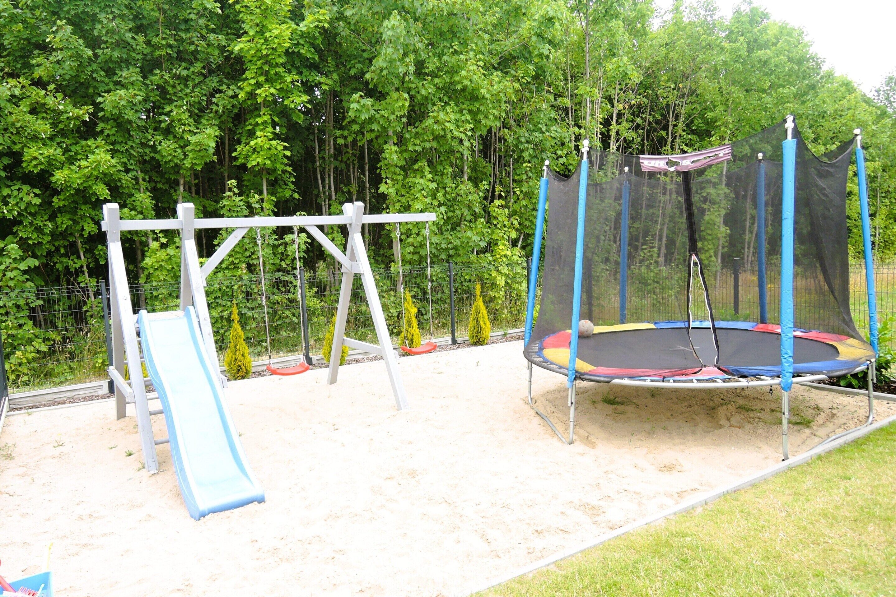 A playground with a slide, swing set, and trampoline.