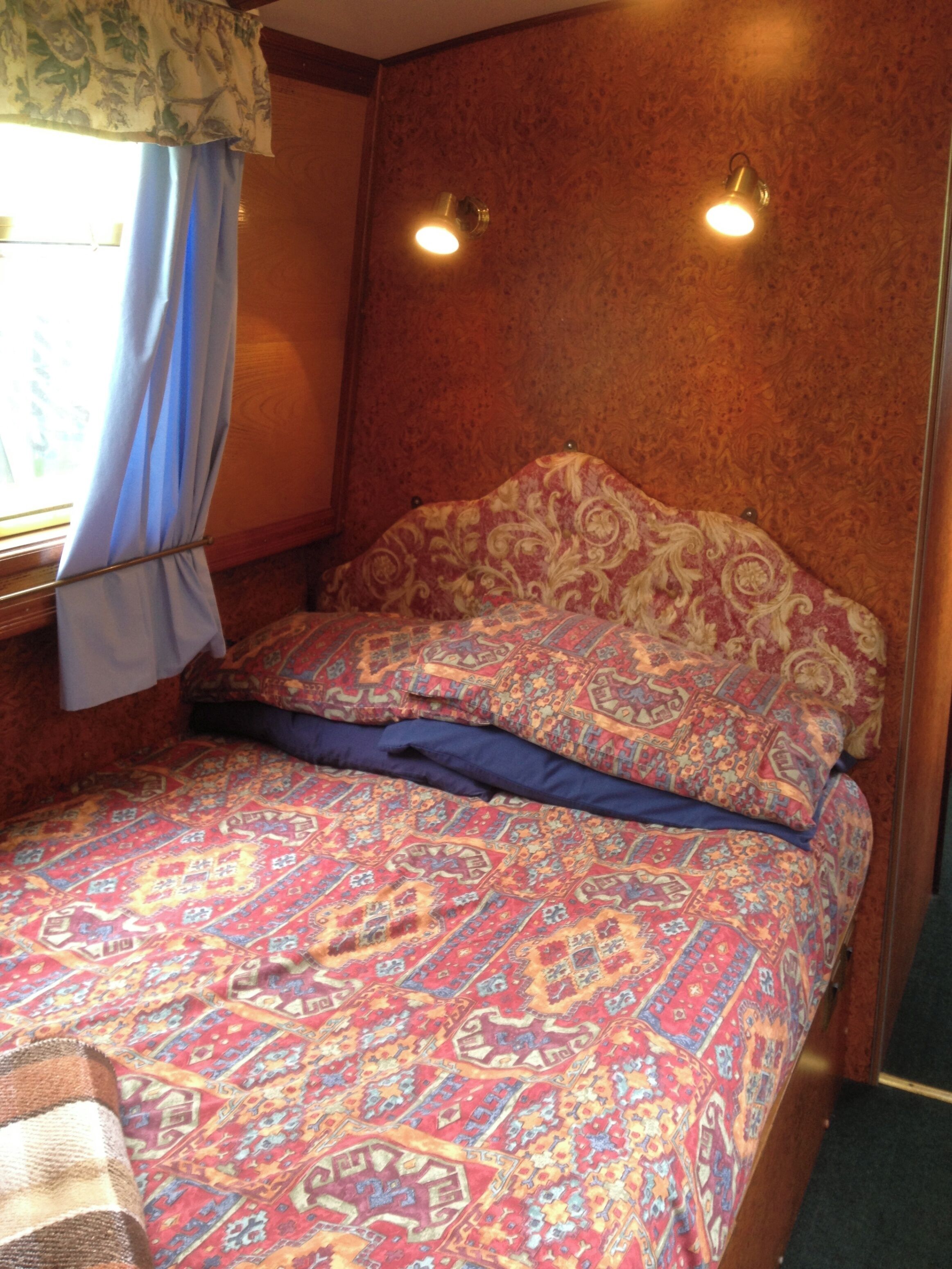 A bed with patterned bedding, a window with curtains, and two wall-mounted lights.