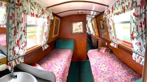 A compact RV interior with two beds, a small sink, and floral curtains. - Stone - Boat - Sleeps 6 - Pet Friendly - 85ws (Stone)