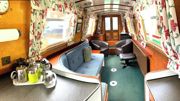 A cozy interior with a blue sofa, two black chairs, a wooden table with a kettle and cups, and floral curtains. - Stone - Boat - Sleeps 6 - Pet Friendly - 85ws (Stone)