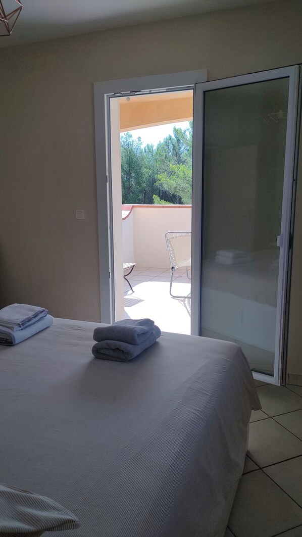 Une chambre d’hôtel avec un lit, une serviette pliée et une vue sur une terrasse extérieure avec des chaises et une table.