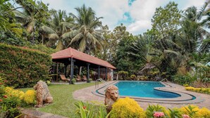 Un área de piscina con zona de estar cubierta, rodeada de exuberante vegetación y palmeras.
