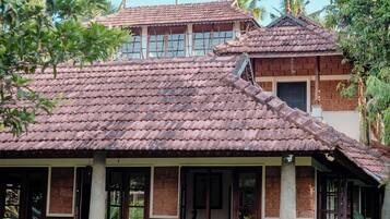 Une maison traditionnelle avec un toit en tuiles, des colonnes en bois et un jardin planté de plantes tropicales.