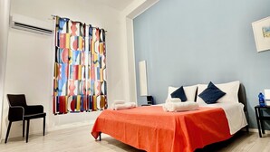A modern hotel room with a large bed, a chair, a colorful curtain, and a blue wall.