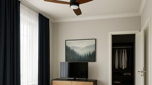 Een slaapkamer met een bed, een televisie op een houten kast, een plafondventilator, een kast en een schilderij aan de muur.