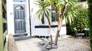A white building with a dark door and a small garden area with a palm tree and a table. - The Mount Street Townhouse (Harrogate)