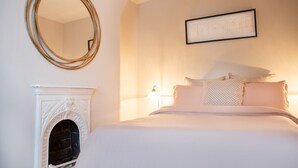 A bedroom with a fireplace, a bed with multiple pillows, a wall-mounted mirror, and a framed picture. - The Mount Street Townhouse (Harrogate)