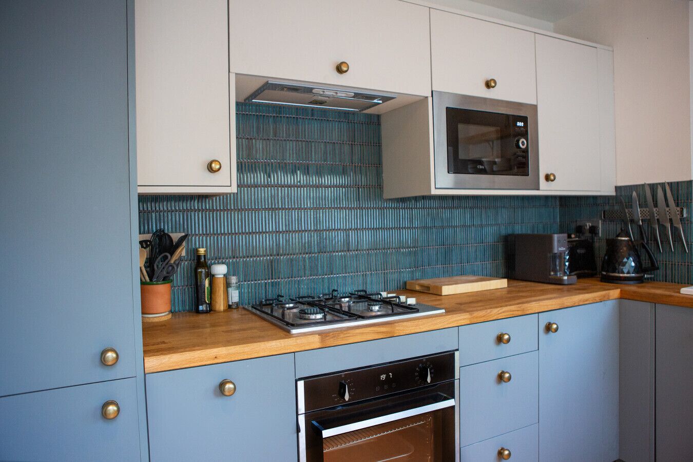 Cucina con piano cottura a gas, forno, microonde e backsplash rivestito di piastrelle blu.