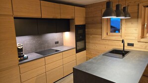 Una cocina moderna con armarios de madera, horno empotrado, lavamanos e iluminación colgante.