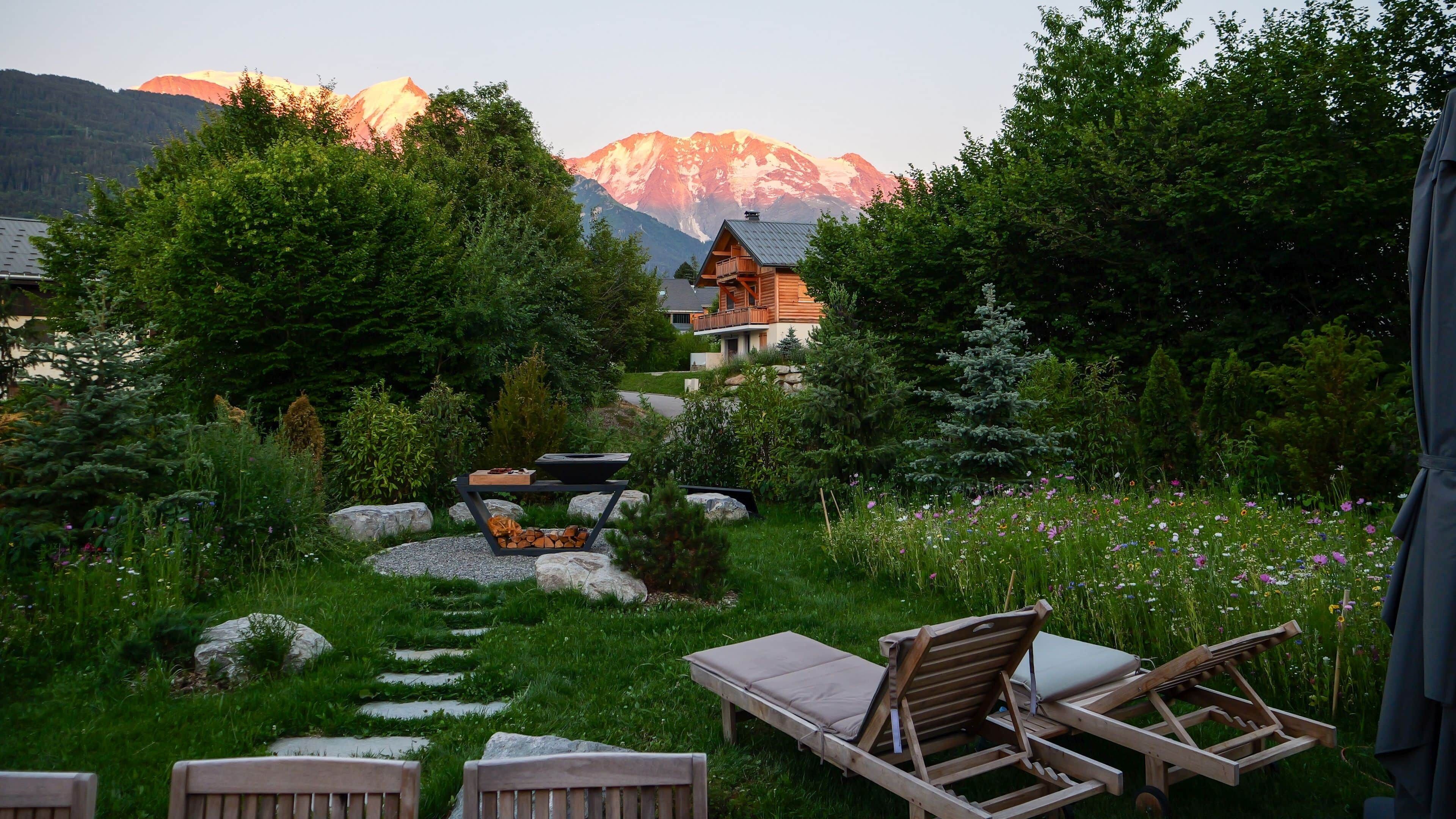 A wooden deck with lounge chairs and a barbecue area, surrounded by a garden with a mountain view.