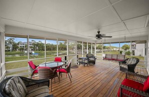 A covered outdoor deck with a table and chairs, a bench, and a view of a lake and buildings. - 419 Tarpon Blvd (Fripp Island)