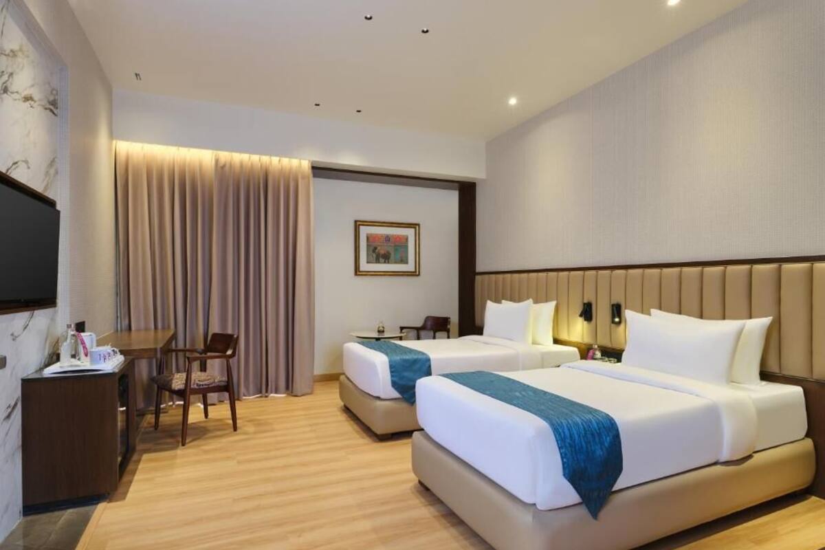 A hotel room with two beds, a desk, a chair, and a television.