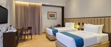 A hotel room with two beds, a desk, a chair, and a television.