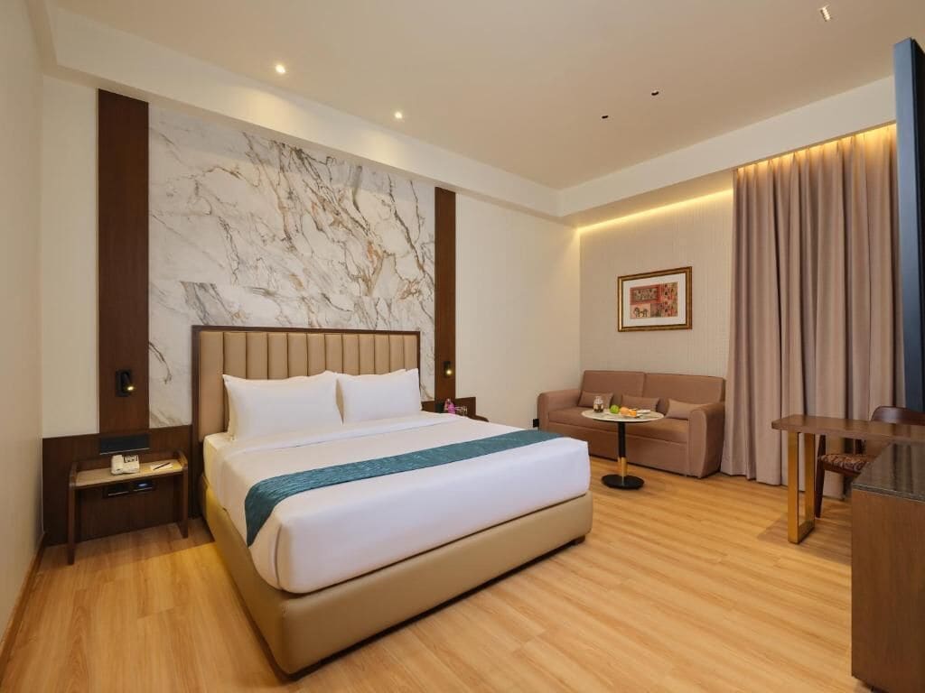 Habitació d'hotel amb un llit gran, un sofà, una taula petita i una televisió.