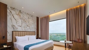 A hotel room with a large bed, a small round table, a chair, a nightstand, and a view of the outdoors. - Regenta Central Shivani Solapur (Mohol)