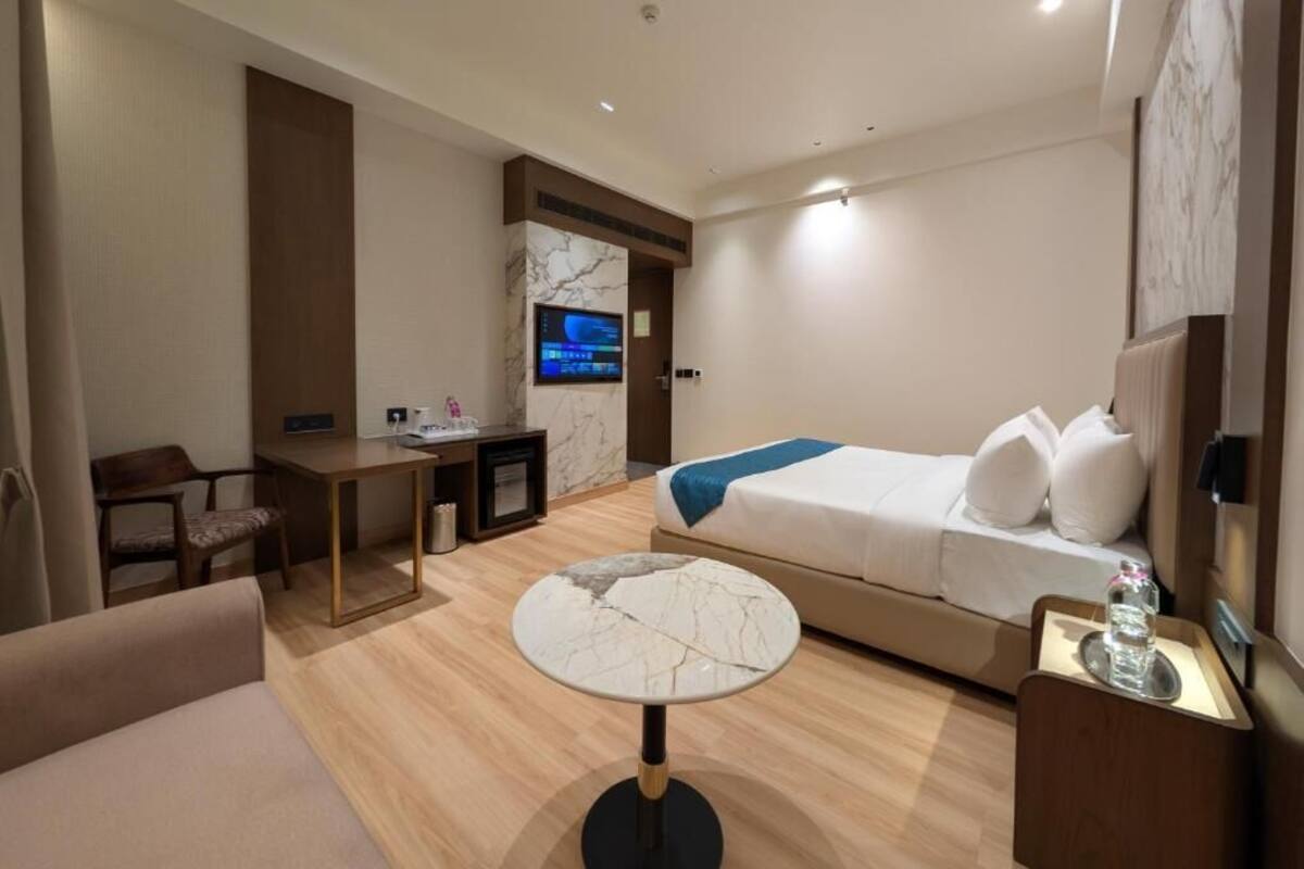 A modern hotel room with a bed, a desk, a chair, a round table, and a television.